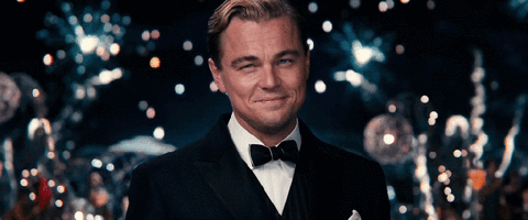 Leonardo DiCaprio in the role of Gatsby in Baz Luhrmann film. He raises a glass of champagne as fireworks erupt behind him.