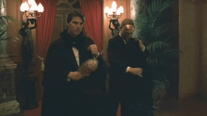Tom Cruise playing Doctor Fridolin steps into an entrance hall in a long black coat and puts on a mask.